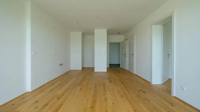 Helles, leeres Zimmer mit neuem Holzfußboden und weißen Wänden, bereit zur individuellen Gestaltung.
