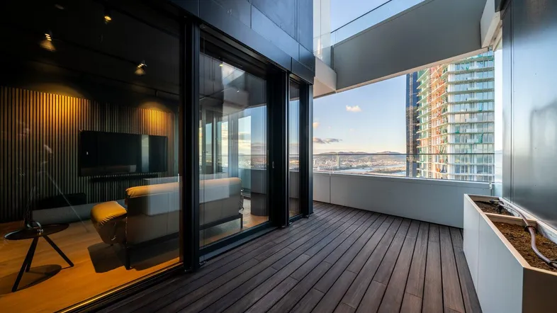 Geräumiger Balkon mit Holzboden, Glasbrüstung und weitem Blick über die Stadt und das Wasser.