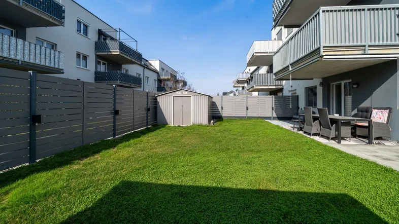 Gepflegter Gartenbereich mit Rasenfläche, Gartenhaus und angrenzender Terrasse zwischen Wohngebäuden.