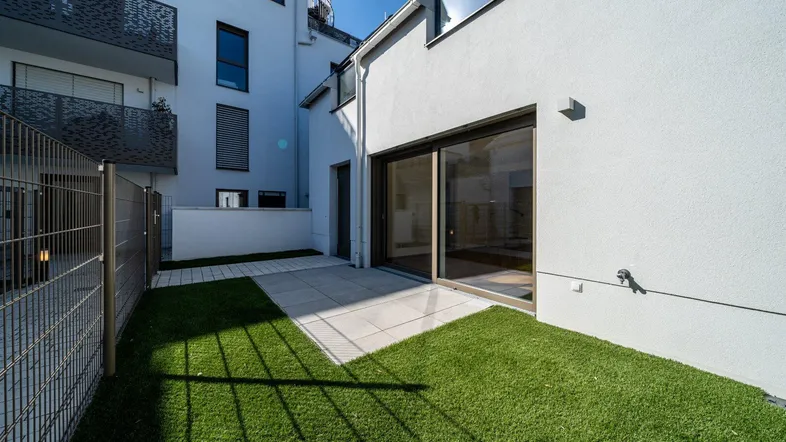 Kleiner privater Gartenbereich mit Kunstrasen und gepflasterter Terrasse, direkt am Gebäude gelegen.