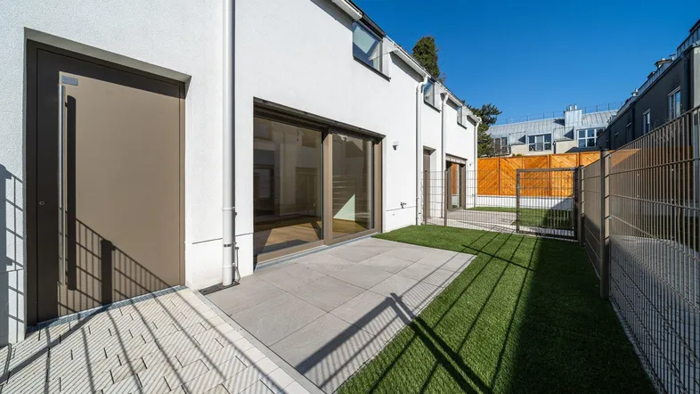 Moderne Reihenhausfassade mit kleiner Terrasse und Kunstrasenfläche im Gartenbereich.