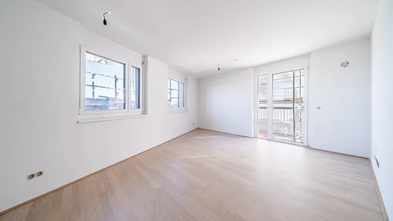 Helles, leeres Zimmer mit hellem Parkettboden und Zugang zu einem Balkon, ideal für Wohnzwecke.