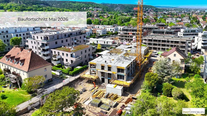 Luftaufnahme einer Baustelle mit umliegenden Wohngebäuden und grüner Landschaft im Hintergrund.
