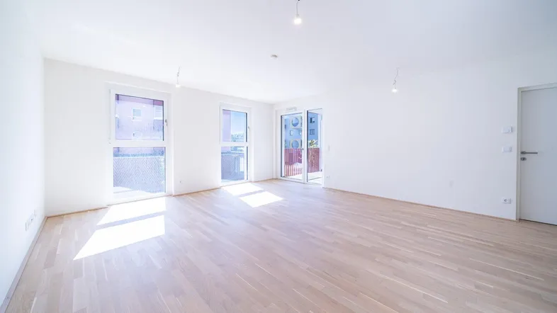 Helles, leeres Wohnzimmer mit Parkettboden und Zugang zu einem Balkon, ideal für neue Mieter.