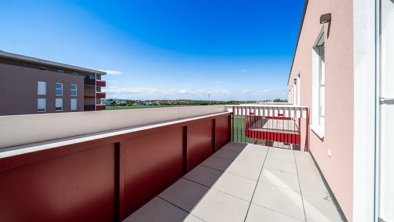 Geräumiger Balkon mit Fliesenboden und weitem Blick über die Landschaft und andere Gebäude.