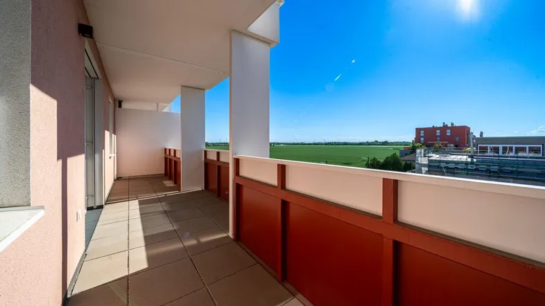 Heller Balkon mit Fliesenboden und rotem Geländer, bietet einen weiten Blick ins Grüne.