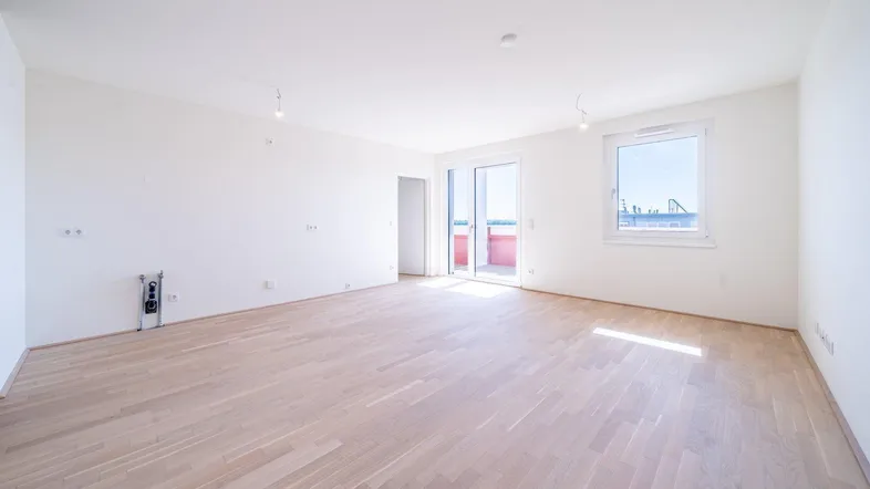 Helles, leeres Wohnzimmer mit Parkettboden und Zugang zu einem Balkon, ideal für individuelle Gestaltung.
