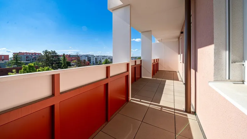 Langer, sonniger Balkon mit rotem Geländer und Blick auf die Stadt.