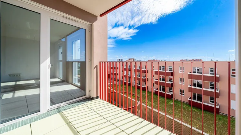 Heller Balkon mit rotem Geländer und Blick auf die umliegenden Wohngebäude und den Innenhof.