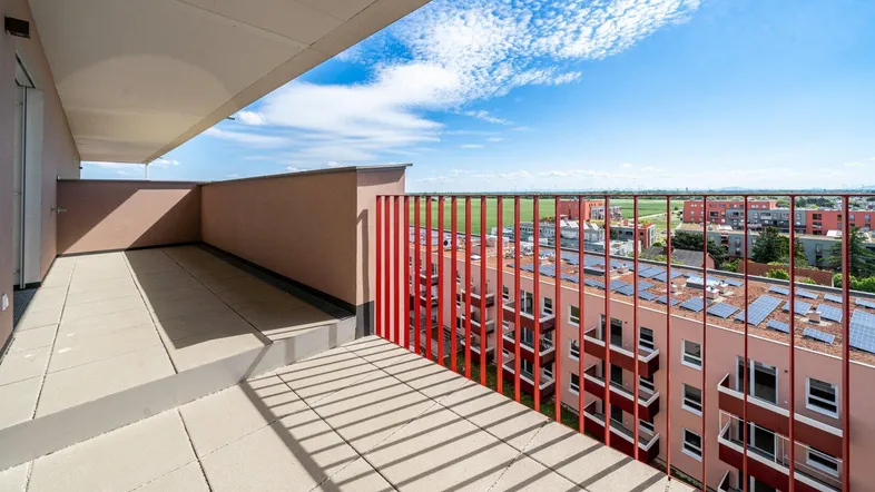 Geräumige Terrasse mit Fliesenboden, rotem Geländer und weitem Blick über die Umgebung.