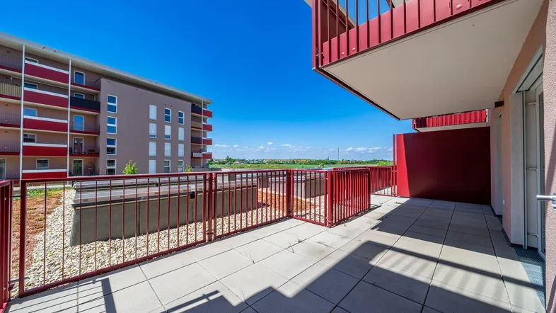 Geräumige Terrasse mit roten Geländern und Blick auf umliegende Gebäude und die Ferne.
