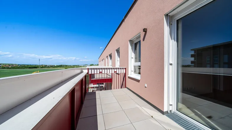 Geräumige Terrasse mit Fliesenboden und rotem Geländer, bietet einen weiten Blick ins Grüne.
