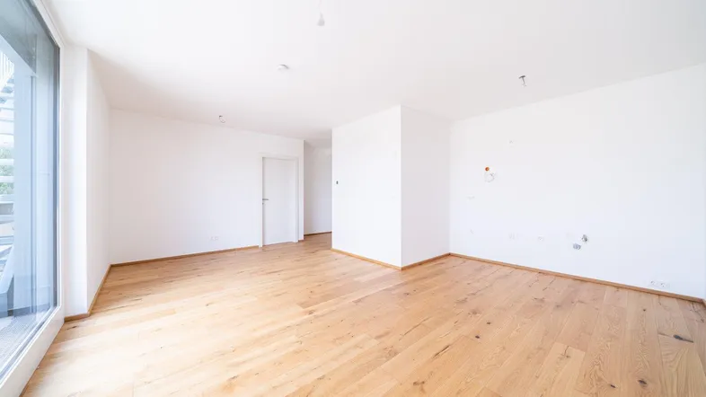 Lichtdurchfluteter Raum mit großen Fenstern und neuem Holzboden, ideal für ein Wohnzimmer.