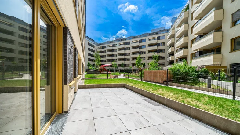 Große gepflasterte Terrasse mit Blick auf den begrünten Innenhof und moderne Wohngebäude.