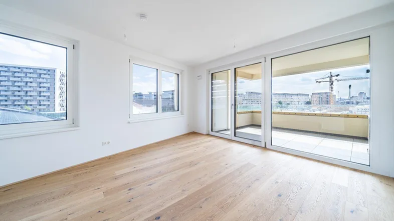 Helles, leeres Zimmer mit Holzboden und Zugang zu einem Balkon, bietet einen weiten Blick.