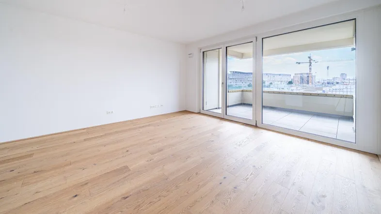 Helles, leeres Zimmer mit Parkettboden und Zugang zu einem Balkon, ideal als Wohnbereich.