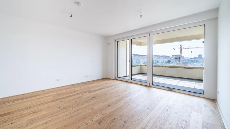 Helles Zimmer mit Holzboden und Zugang zu einem Balkon mit Stadtblick und Baustelle.