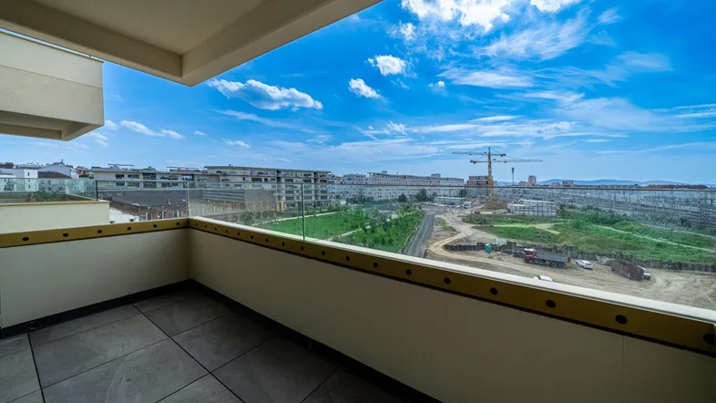 Geräumiger Balkon mit Fliesenboden und Glasgeländer, bietet einen weiten Blick über die Stadt und Baustellen.