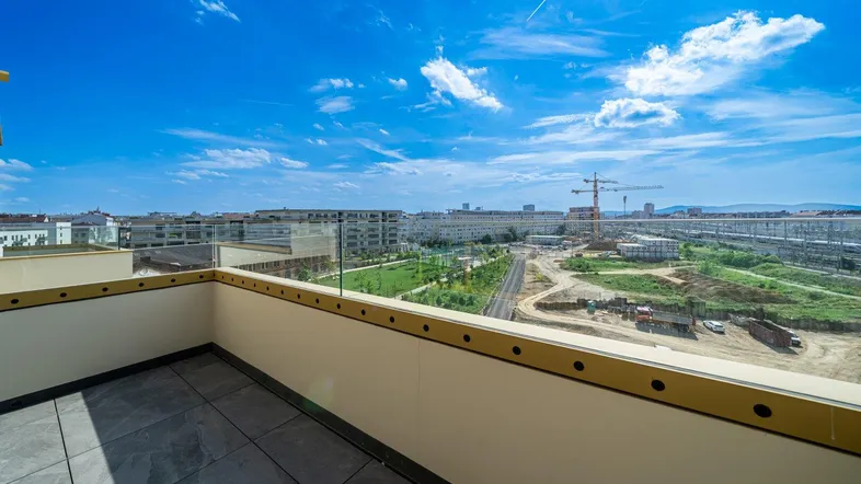 Geräumiger Balkon mit Fliesenboden und weitem Blick über die Stadt und Baustellen.