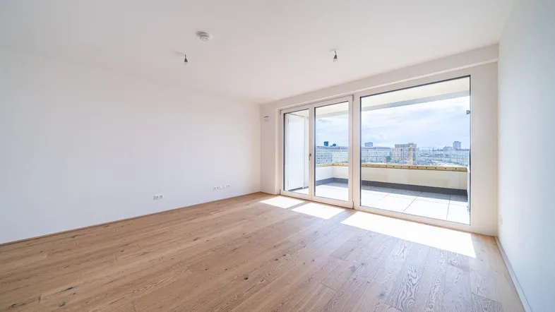 Helles Zimmer mit Holzboden und großen Schiebetüren, die auf einen Balkon mit Stadtblick führen.