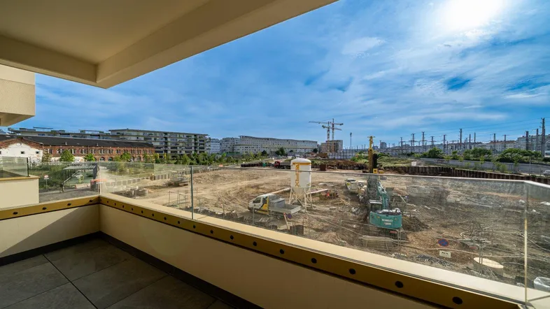 Geräumiger Balkon mit Glasbrüstung und Blick auf eine Baustelle unter blauem Himmel.