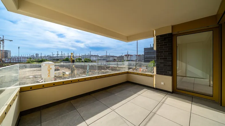 Geräumiger Balkon mit Fliesenboden und Glasgeländer, bietet einen weiten Blick auf die Stadt und Baustellen.
