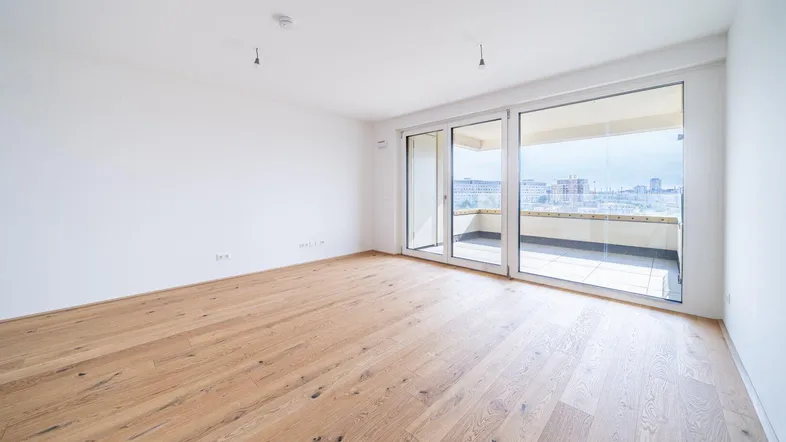 Helles, leeres Zimmer mit Holzboden und Zugang zu einem großen Balkon.