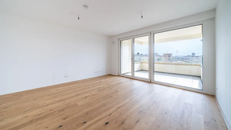 Helles, leeres Zimmer mit Holzboden und Zugang zu einem Balkon, bietet viel natürliches Licht.