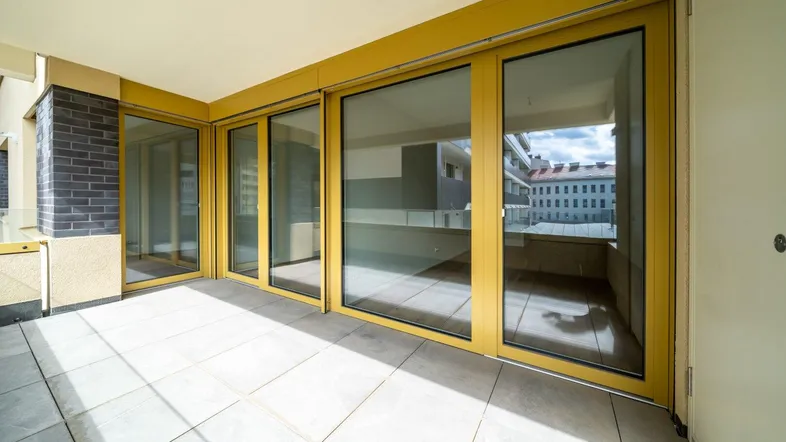 Geräumiger Balkon mit Fliesenboden und gelben Fensterrahmen, bietet einen Blick auf die Umgebung.