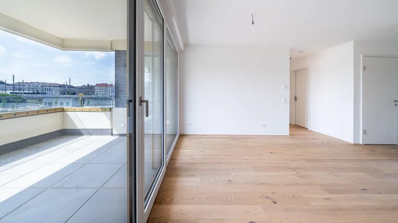 Helles Wohnzimmer mit Holzboden und großen Schiebetüren, die zu einem Balkon mit Flussblick führen.