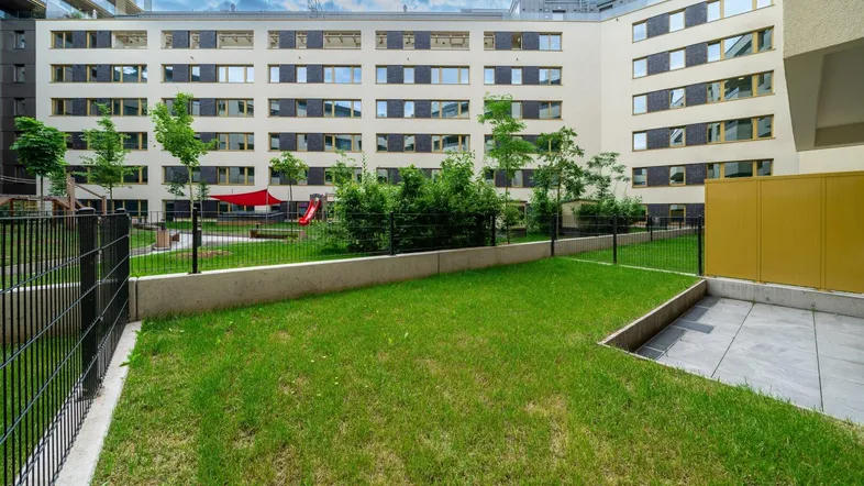 Außenansicht eines modernen Wohngebäudes mit gepflegtem Rasen und Kinderspielplatz im Innenhof.
