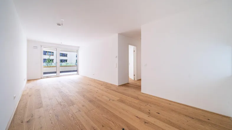 Helles, leeres Zimmer mit Holzboden und Zugang zu einem Balkon, bereit zur individuellen Gestaltung.