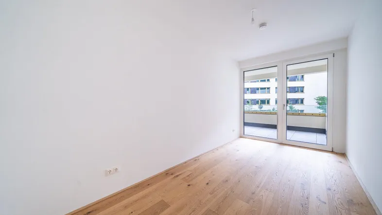 Helles Zimmer mit Holzboden und Zugang zu einem Balkon, ideal als Schlafzimmer nutzbar.