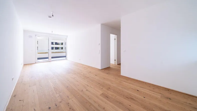 Helles, leeres Wohnzimmer mit neuem Parkettboden und Zugang zu einem Außenbereich, bereit zum Einzug.