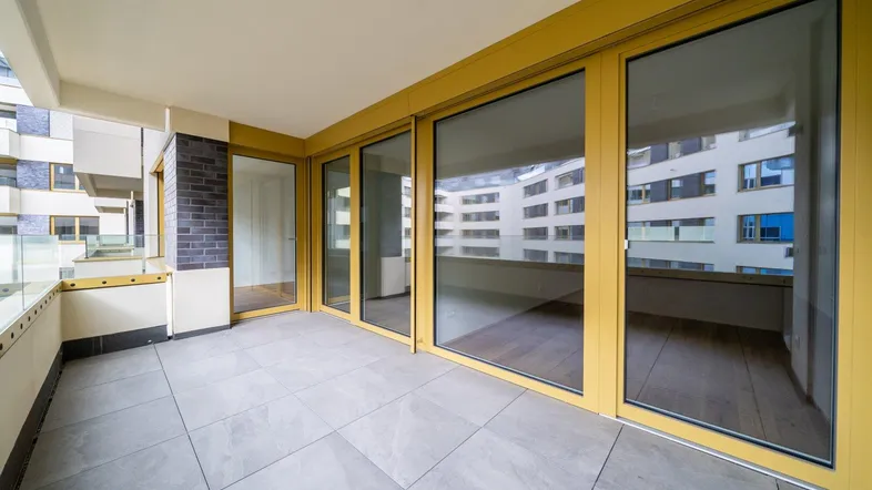 Großer Balkon mit Fliesenboden und Glasgeländer, bietet Zugang zu den hellen Innenräumen.