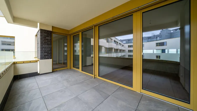 Geräumiger Balkon mit Fliesenboden und Glasgeländer, bietet einen Blick auf die umliegenden Gebäude.