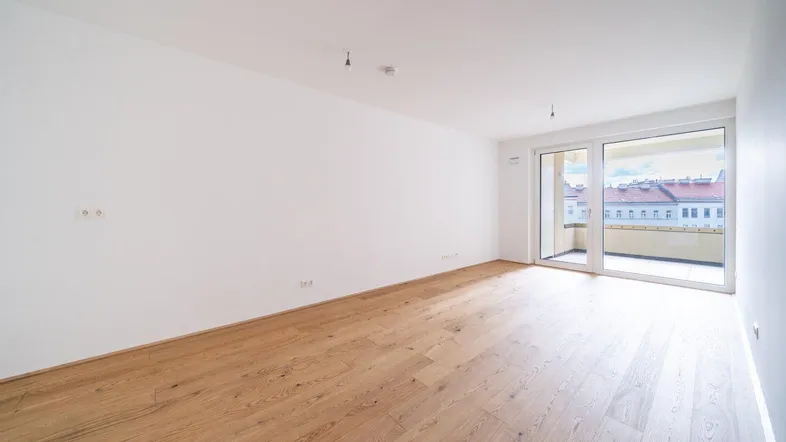 Helles Zimmer mit Parkettboden und Zugang zu einem Balkon, ideal als Wohn- oder Schlafbereich.