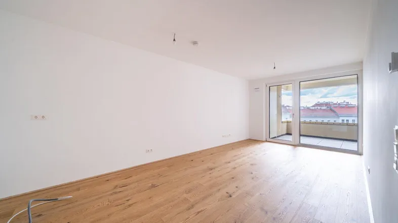 Helles, leeres Wohnzimmer mit Holzboden und Zugang zu einem Balkon mit Stadtblick.