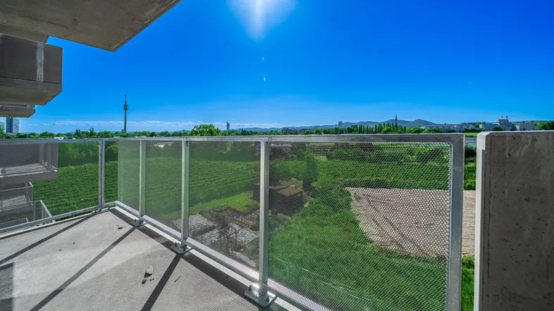Heller Balkon mit weitem Blick über grüne Felder und die Stadt bei Sonnenschein.