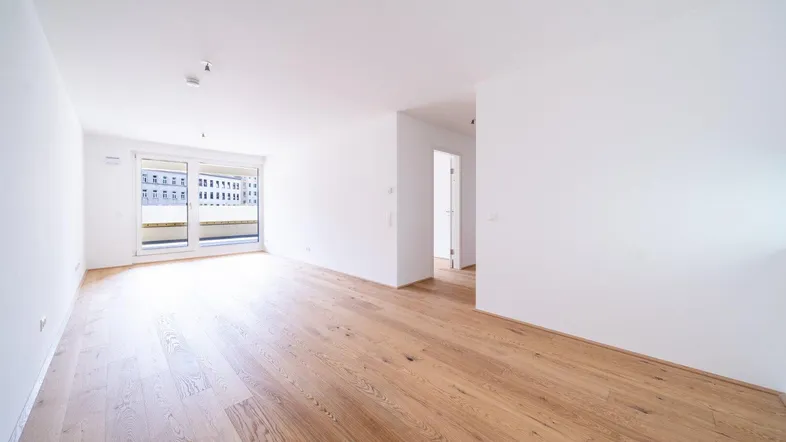 Helles, leeres Zimmer mit neuem Parkettboden und großen Fenstern, die viel Tageslicht hereinlassen.