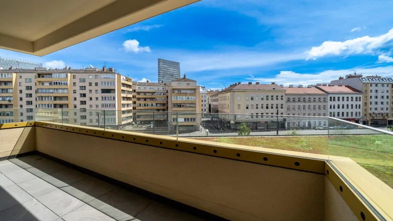 Geräumiger Balkon mit Glasgeländer und weitem Blick über die Stadt unter blauem Himmel.
