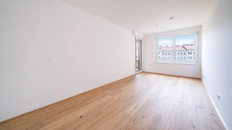 Helles, unmöbliertes Zimmer mit Parkettboden und großen Fenstern, die viel Tageslicht hereinlassen.