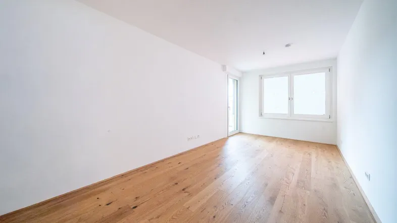 Helles, leeres Zimmer mit weiß gestrichenen Wänden und schönem Holzparkettboden, bereit zum Einzug.