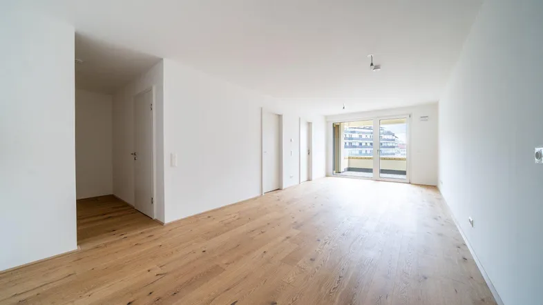 Helles, leeres Zimmer mit neuem Parkettboden und Zugang zu einem Balkon, bereit zur individuellen Gestaltung.