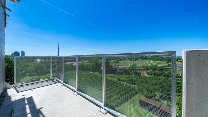 Geräumiger Balkon im Bau mit weitem Blick über Weinberge und die Stadt in der Ferne.