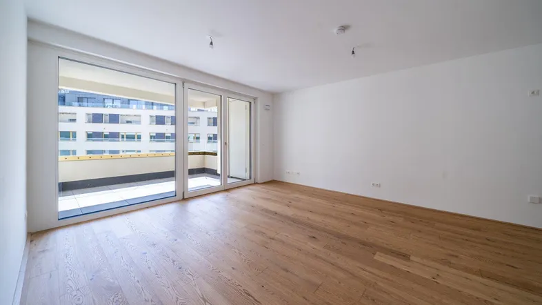 Helles, unmöbliertes Zimmer mit Holzboden und großem Zugang zu einem Balkon.