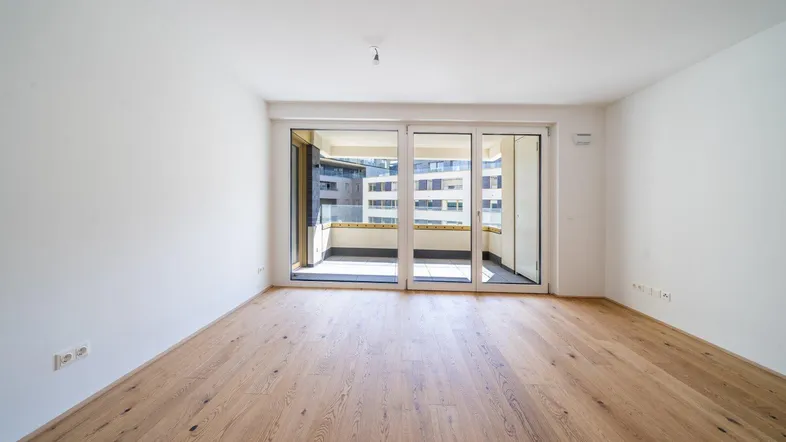 Helles Zimmer mit Holzboden und großen Schiebetüren, die auf einen Balkon führen.