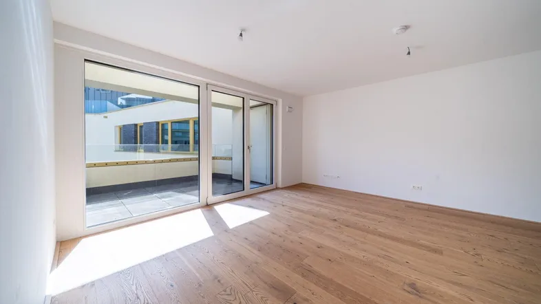 Helles Zimmer mit Holzboden und Zugang zu einem Balkon, ideal als Wohn- oder Schlafbereich.
