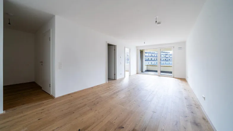 Helles, leeres Wohnzimmer mit Parkettboden und Zugang zu einem Balkon, bereit zur individuellen Gestaltung.
