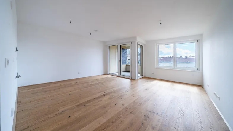 Helles, leeres Zimmer mit schönem Holzparkettboden und Zugang zu einem Balkon.